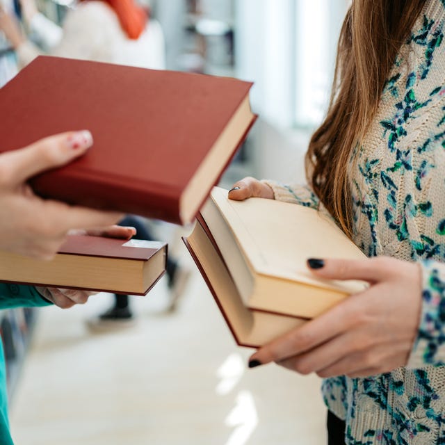 two female students exchanging books in a student library in college. close up.