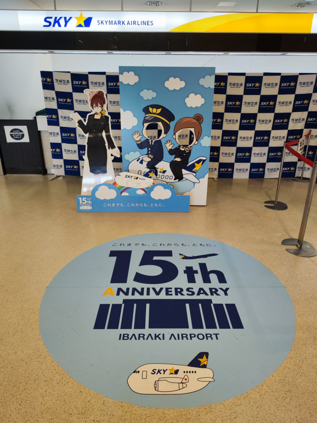 ニュース画像 6枚目：スカイマークのカウンター付近の顔ハメパネルと、開港15周年を祝う表示 2025年撮影