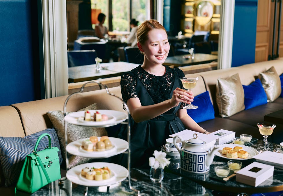 afternoon tea setup featuring a woman holding a cocktail and an assortment of pastries afternoon tea setup featuring a woman holding a cocktail and an assortment of pastries
