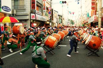 緑の衣装にはちまきをした人たちが和太鼓を披露している写真