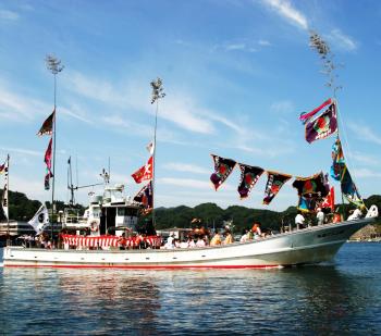 大漁旗が飾られた船に乗り曳船まつりが行われている様子の写真