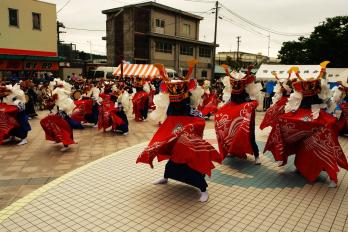赤と白の衣装を着てお面をがぶった人たちが踊りをしている様子の写真