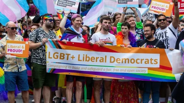 「LGBT+の自由民主党員」と書かれた横断幕を掲げて更新する人々
