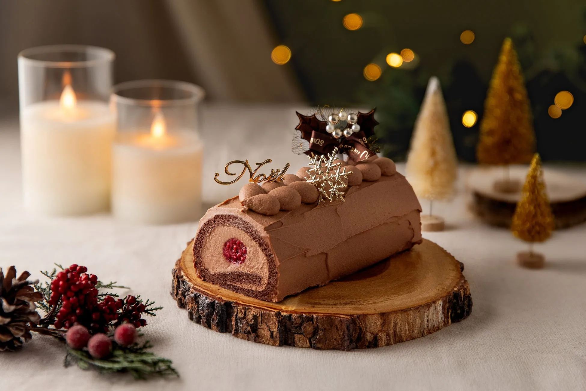 クリスマスのチョコレートケーキの写真です。ケーキの上には「Noël」の飾りと雪の結晶の飾りがあり、周りにはキャンドルやクリスマスツリーが配置されています。