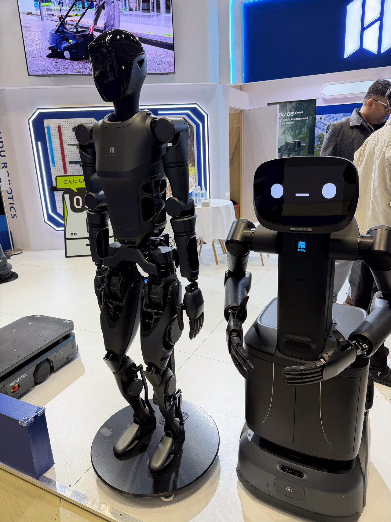 左が二足歩行の人型ロボット「PUDU D9」、右がセミヒューマノイドの「FlashBot Arm」。FlashBot Armは配送ロボットに2本のアームを追加した構成で、エレベーター操作やカードキー認証を自律で行える